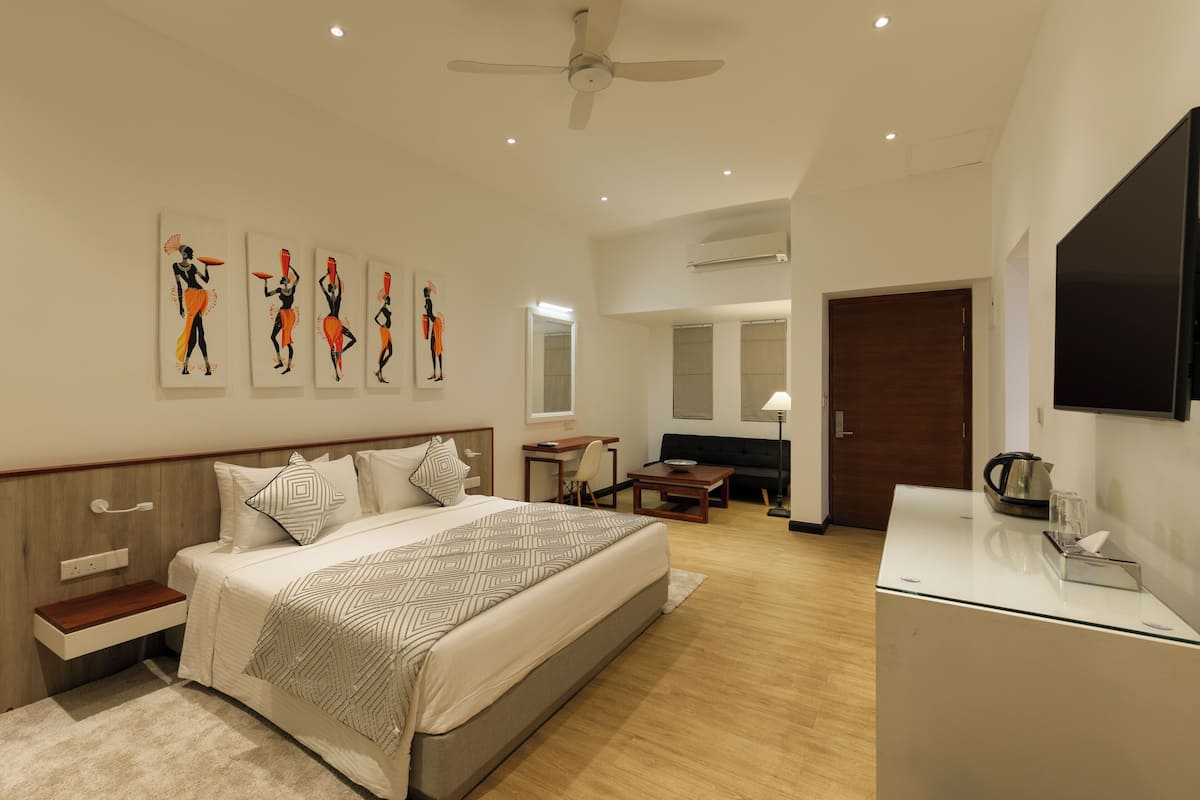 A modern hotel room with a large bed, a desk, a flat-screen TV, and artwork on the wall.