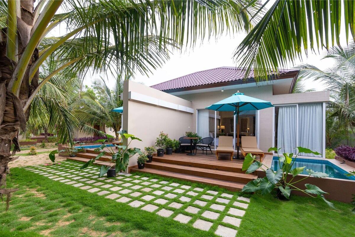 A two-story building with a swimming pool, outdoor seating, and lush greenery.