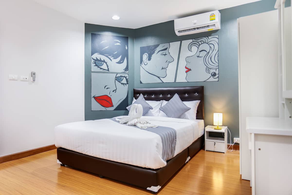 A modern hotel room with a large bed, a nightstand with a lamp, and artwork on the walls.