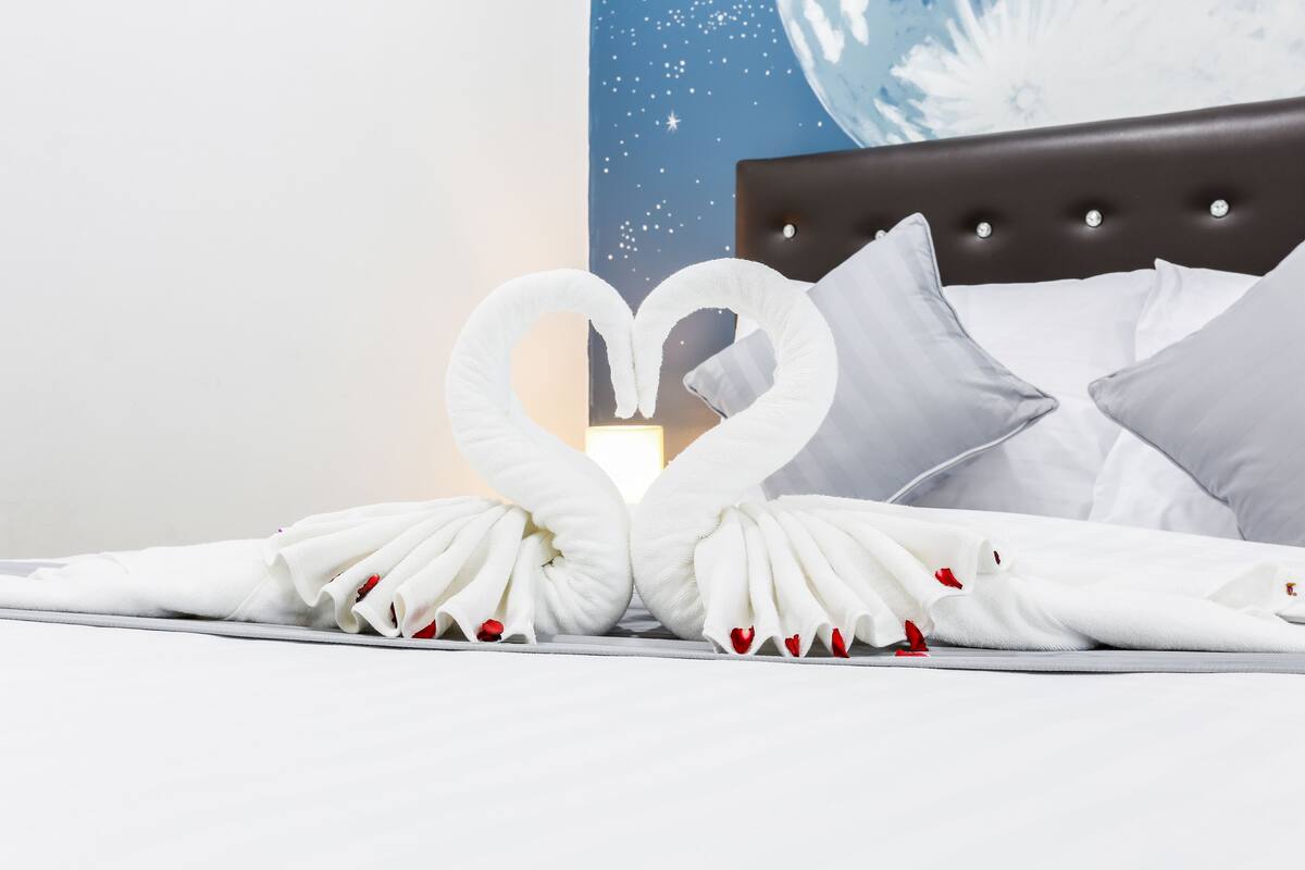 A bed with white pillows and a heart-shaped towel arrangement.