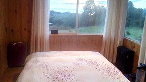 A room with a large bed, wooden walls, a window with curtains, and a view of the outdoors.