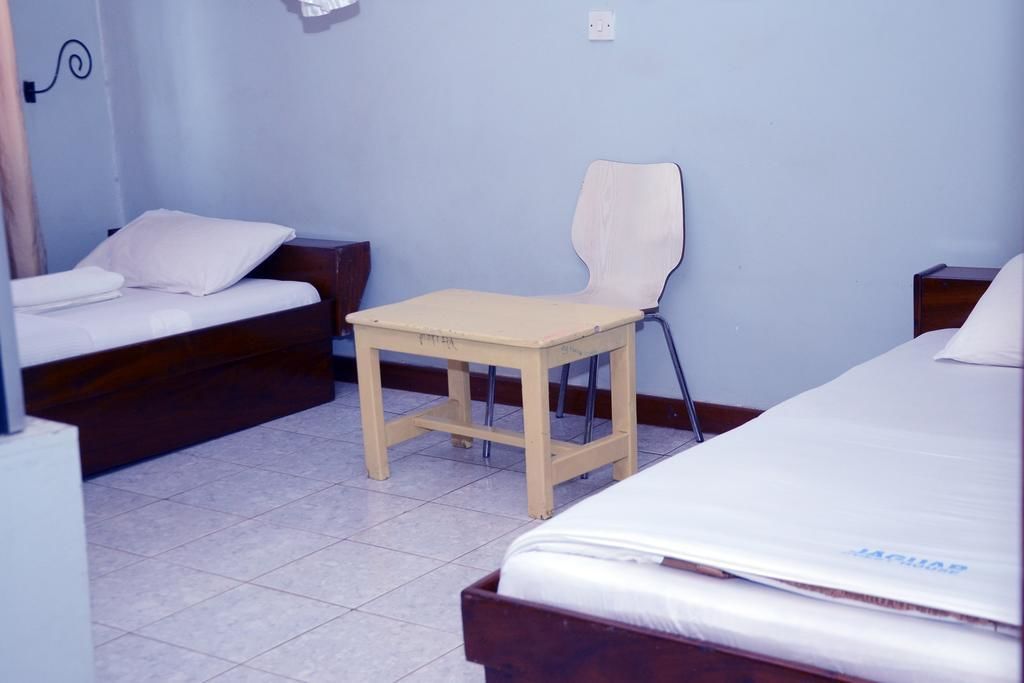 A room with two beds, a small wooden table, and a chair.