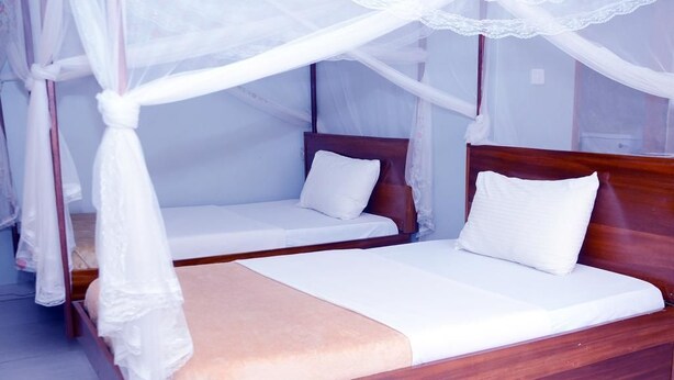 A double bed with a wooden headboard and a canopy. - Jaguar Guest House (Kampala)