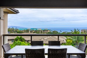 A balcony with a table and chairs, overlooking a coastal area with buildings and a view of the ocean. - I.P.M PRESENTS: HOOLEI 99-2 BRAND NEW REMODEL - WOW! FLEXIBLE CANCELATION POLICY (Kihei)