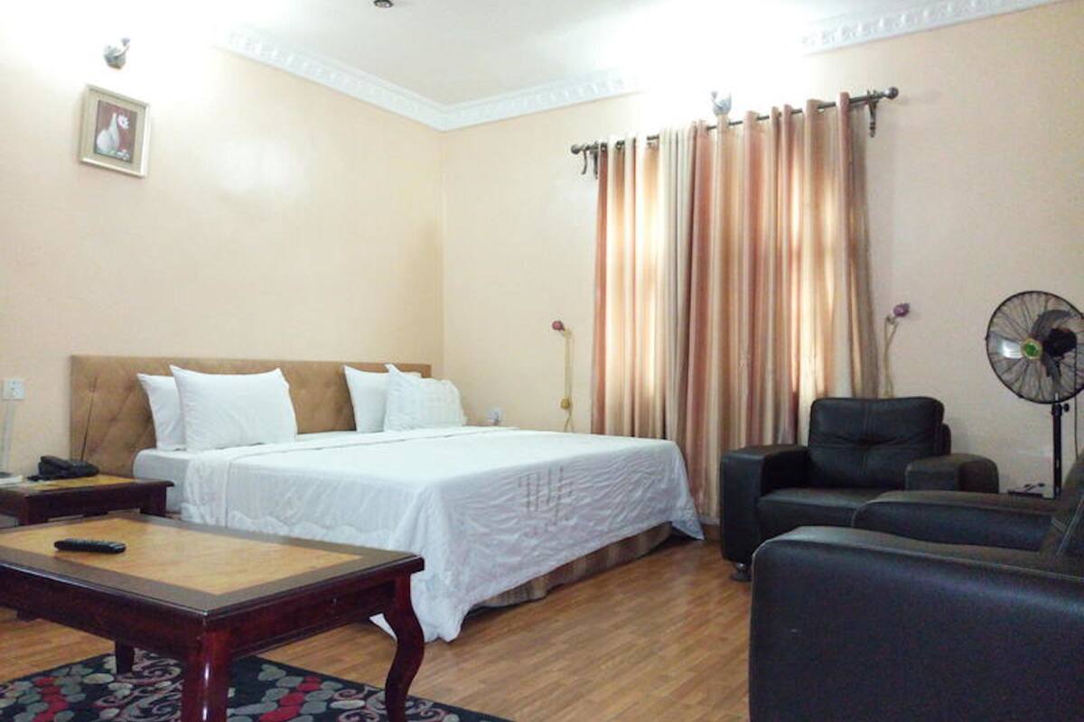 A hotel room with a bed, a desk, a chair, a fan, and curtains.