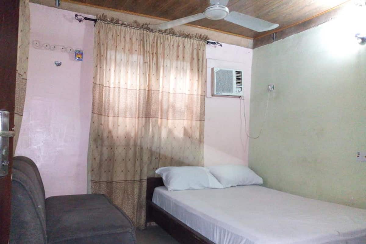 A small, single-bed room with a ceiling fan, a window with an air conditioning unit, and a couch.