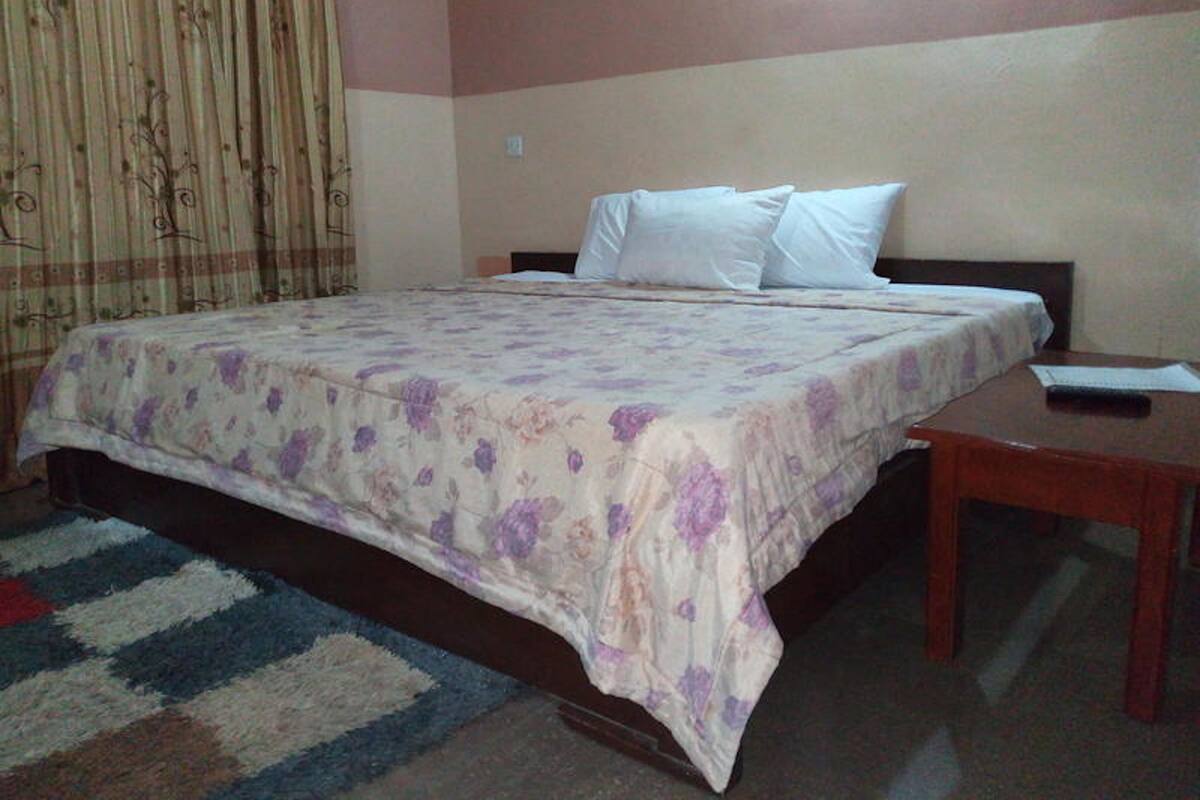 A single bed with a floral bedspread, a wooden nightstand, and a patterned rug.