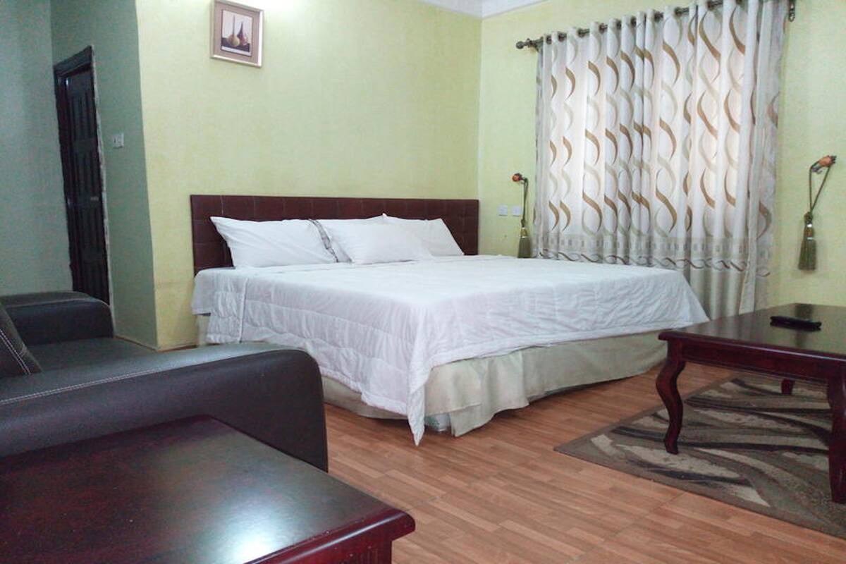 A hotel room with a bed, a wooden table, a sofa, and a patterned curtain.