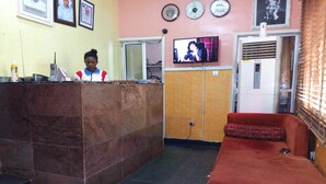 Una zona d' recepció amb un taulell de marbre, un televisor penjat a la paret i un sofà vermell.
