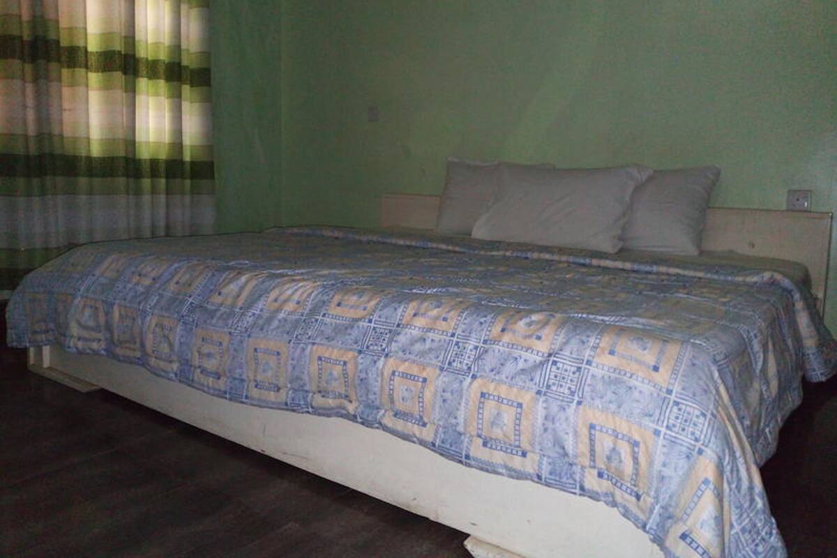 A single-bed room with a patterned bedspread, green walls, and a wooden floor.