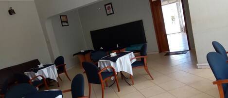 A conference room with tables and chairs, a large flat-screen TV, and a door leading outside.
