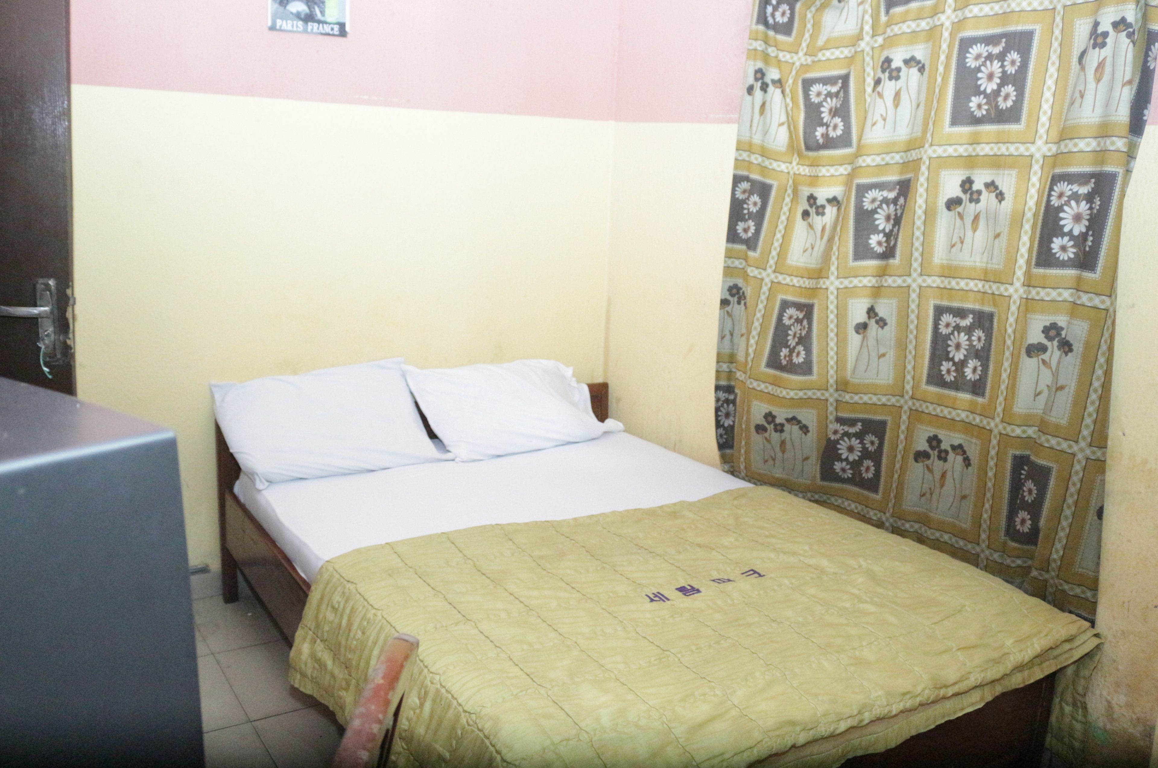 A single bed with a yellow bedspread and white pillows in a room with a pink and yellow wall.