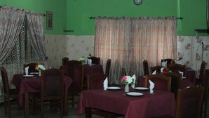 Zona de dinar amb taules preparades per a quatre, cadascuna amb mantell vermell, plats blancs i un ram de flors.