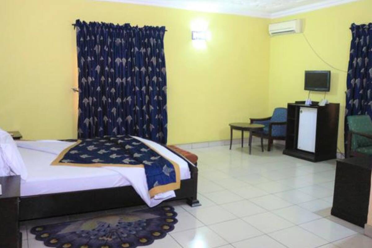 A hotel room with a bed, a desk, a chair, a television, and an air conditioning unit.