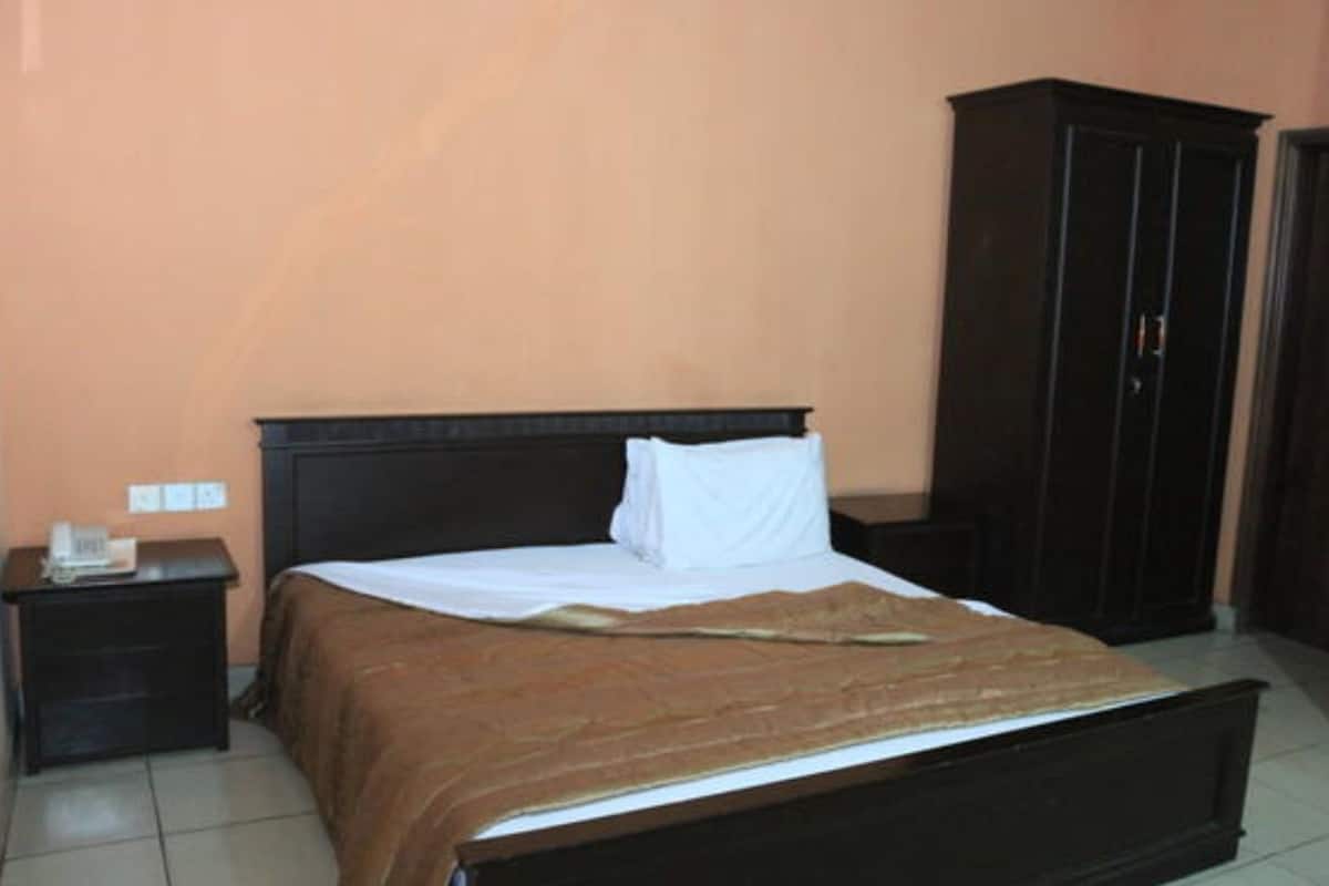A bedroom with a bed, a nightstand, a wardrobe, and a wall socket.