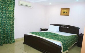 A bedroom with a bed, a nightstand, a wall-mounted air conditioner, and a framed picture on the wall. - Golf Prince Hotel (Port Harcourt)