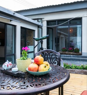 A table with a telescope, a potted plant, a bowl of fruit, and a teapot on a patio. - Beijing Ru Xi Inn (Huairou)