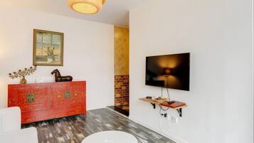 Uma sala de estar moderna com um armário vermelho, uma mesa redonda branca, uma TV fixada na parede e um lustre.