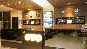 A hotel reception area with a reception desk labeled "OYO," a large screen displaying images, clocks indicating different time zones, and a polished floor. - Prime Royal Boutique Hotel (Surabaya)