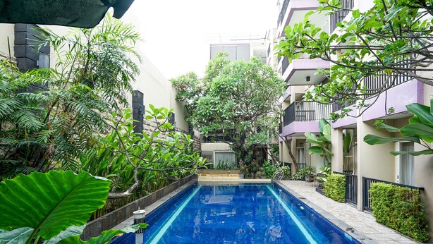 A swimming pool surrounded by lush greenery and multi-story buildings. - Prime Royal Boutique Hotel (Surabaya)