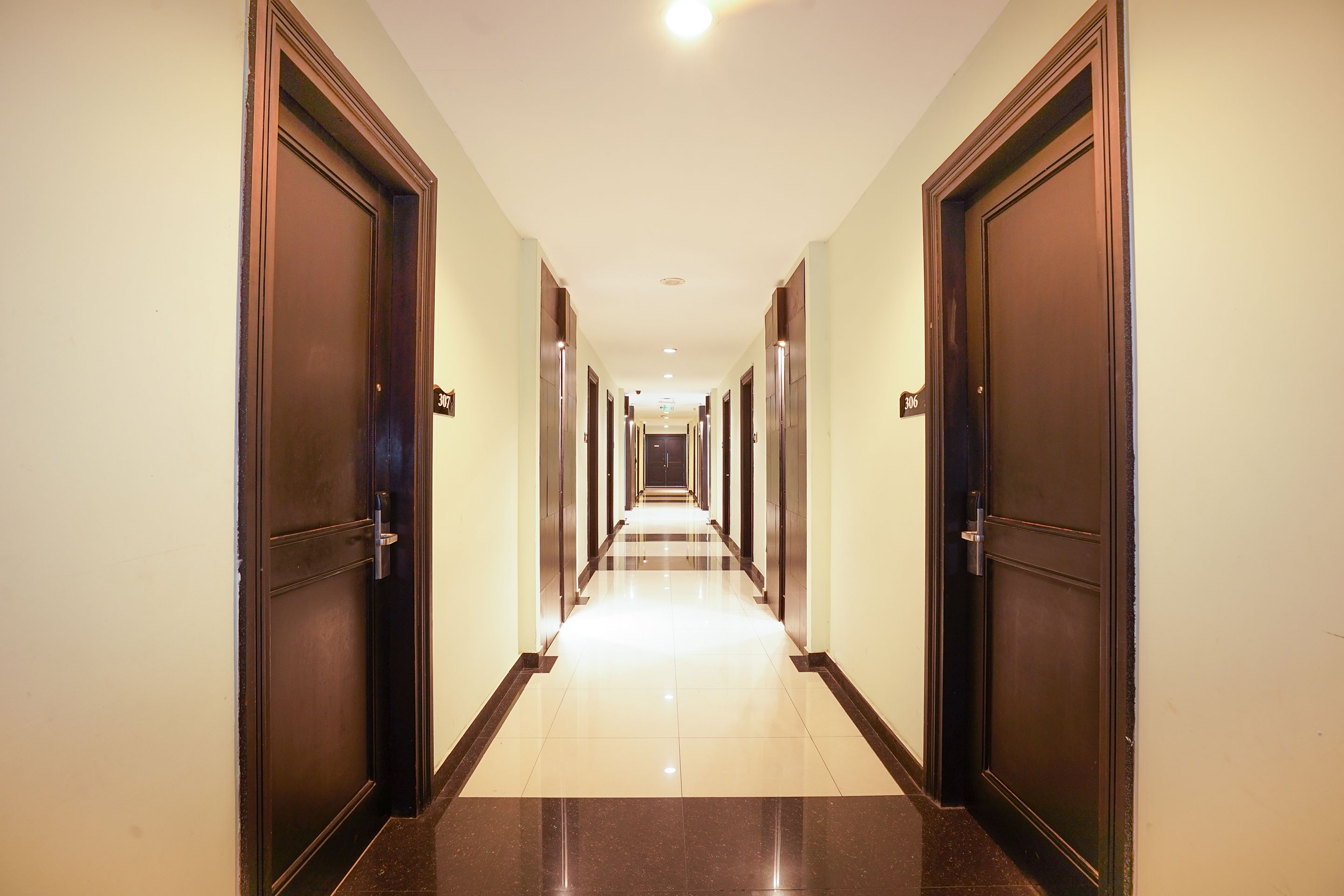 Un largo pasillo bien iluminado con puertas de madera oscura a cada lado, que conduce a varias habitaciones.