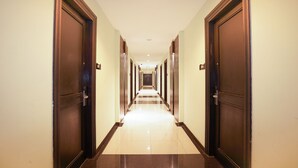 A long, well-lit hallway with dark wooden doors on either side, leading to a series of rooms. - Prime Royal Boutique Hotel (Surabaya)