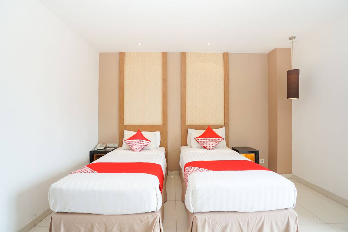 Une chambre d’hôtel avec deux lits, chacun recouvert d’une couverture rouge et blanche, et comprenant un téléphone et une table de chevet.