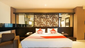 A modern hotel room with a large bed, a brown armchair, and a large mirror. - Prime Royal Boutique Hotel (Surabaya)