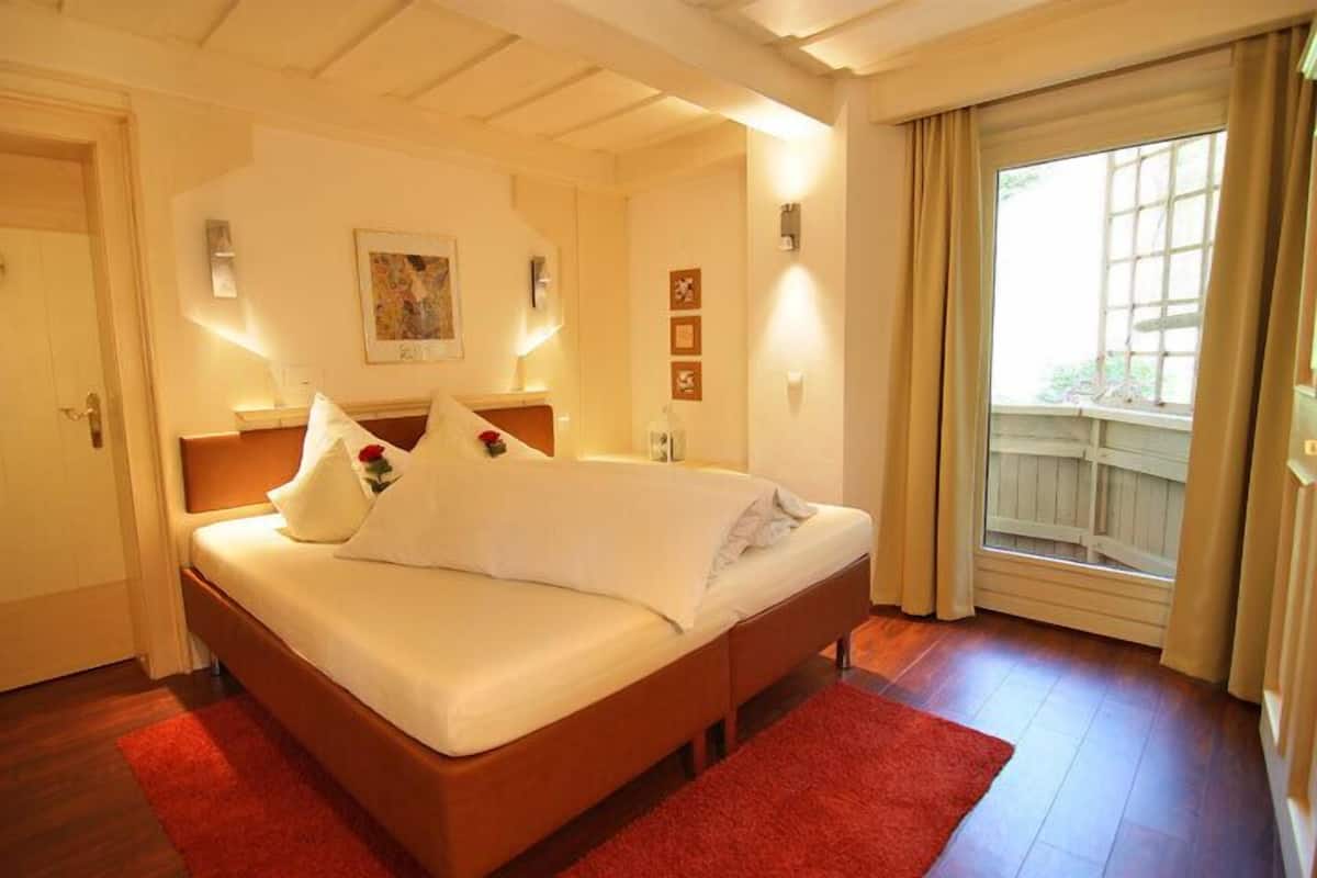 A neatly arranged bedroom with a bed, a window with curtains, and a painting on the wall.