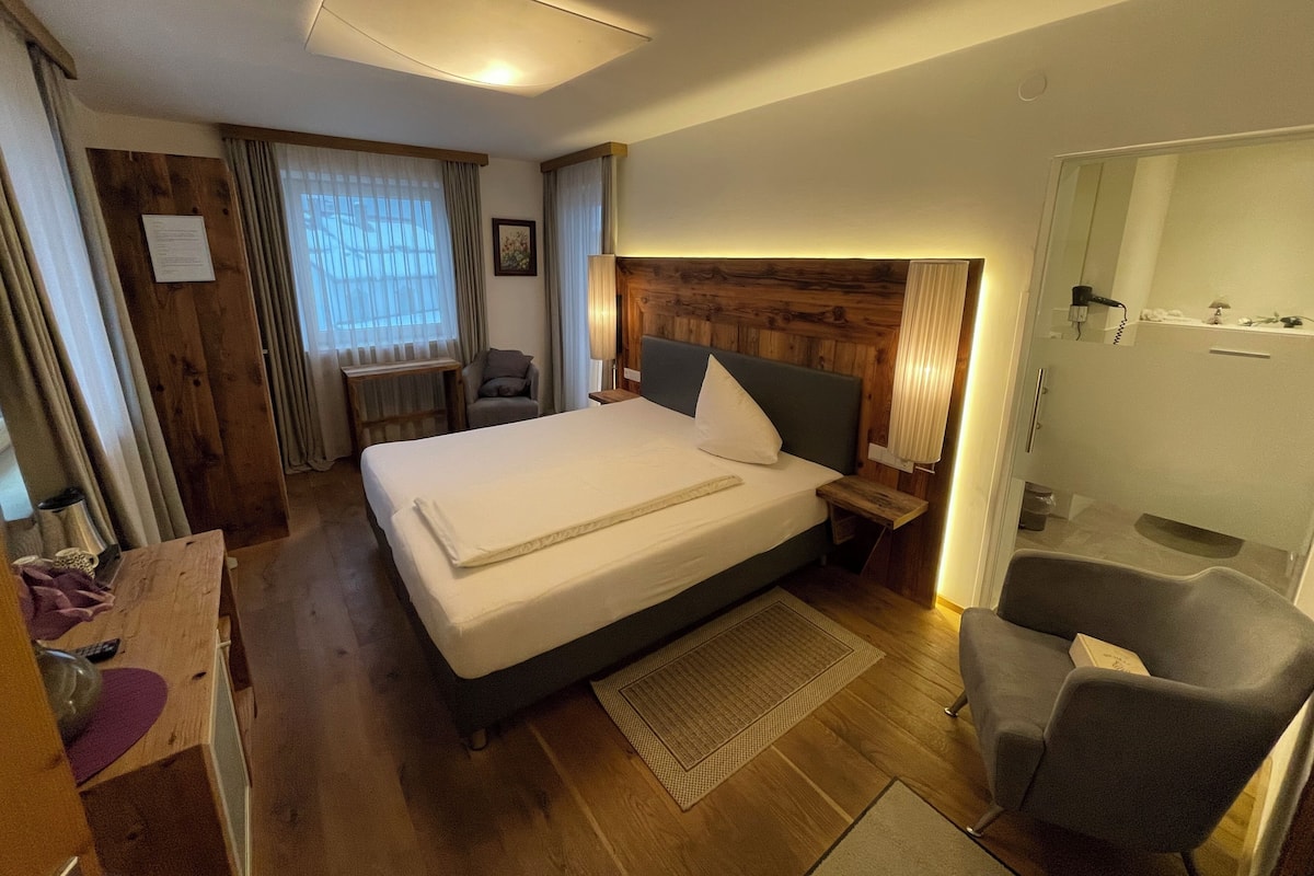 A hotel room with a large bed, wooden headboard, a desk with a chair, a small table, and a mirror.