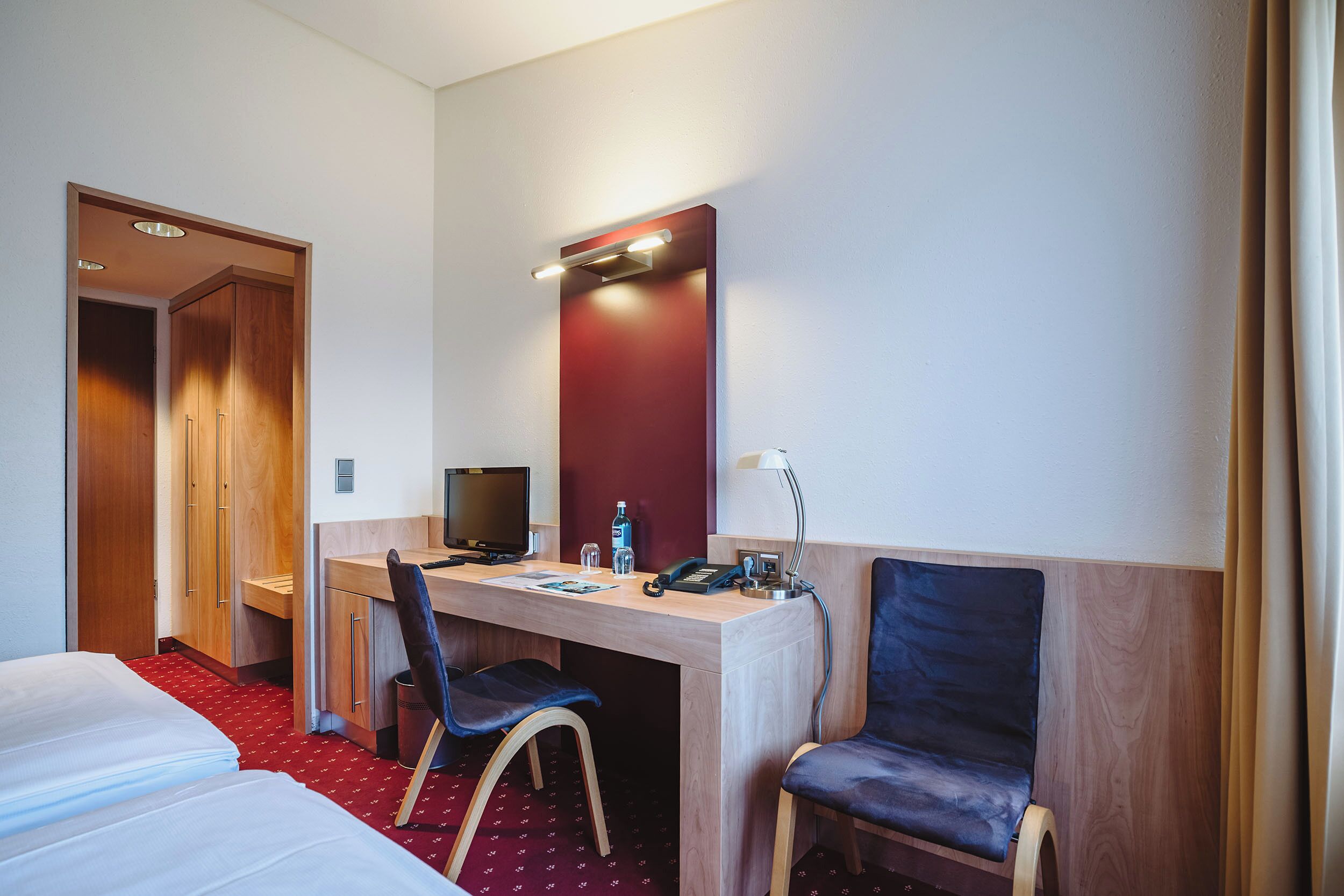 Ein Hotelzimmer mit Bett, Schreibtisch, Stuhl und Spiegel.