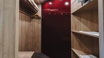 A narrow walk-in closet with wooden shelving, a hanging rack, and a small step leading to a red-lit area.