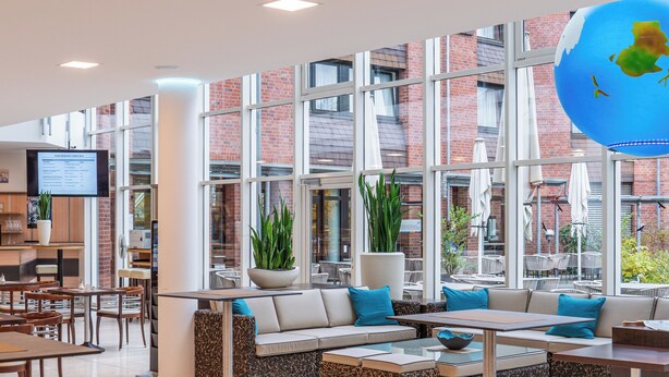 A modern cafe with a bar area, seating arrangements, and large windows offering views of the outside. - Hotel Gustav Stresemann Institut (Bonn)