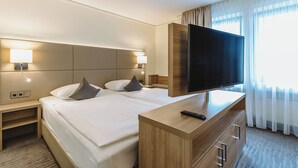 A hotel room with a large bed, a TV on a wooden dresser, and a nightstand with a lamp. - Hotel Gustav Stresemann Institut (Bonn)