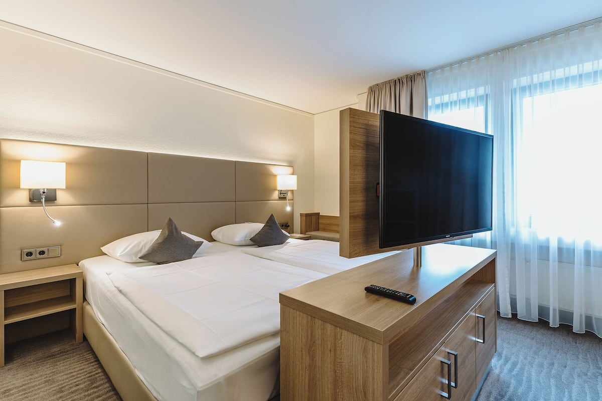 A hotel room with a large bed, a TV on a wooden dresser, and a nightstand with a lamp.