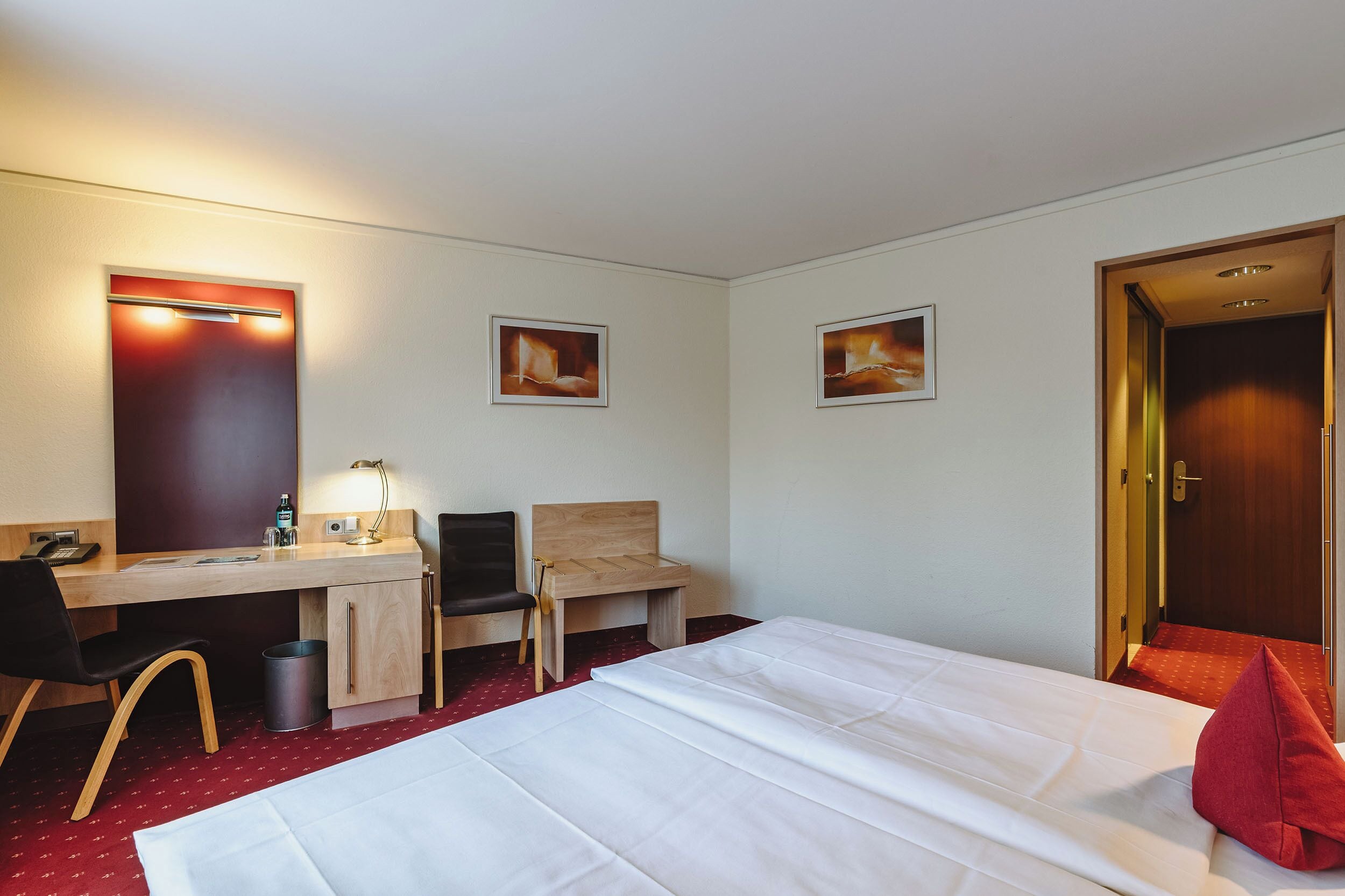 Habitación de hotel con cama, escritorio, silla y una mesita de noche con lámpara.