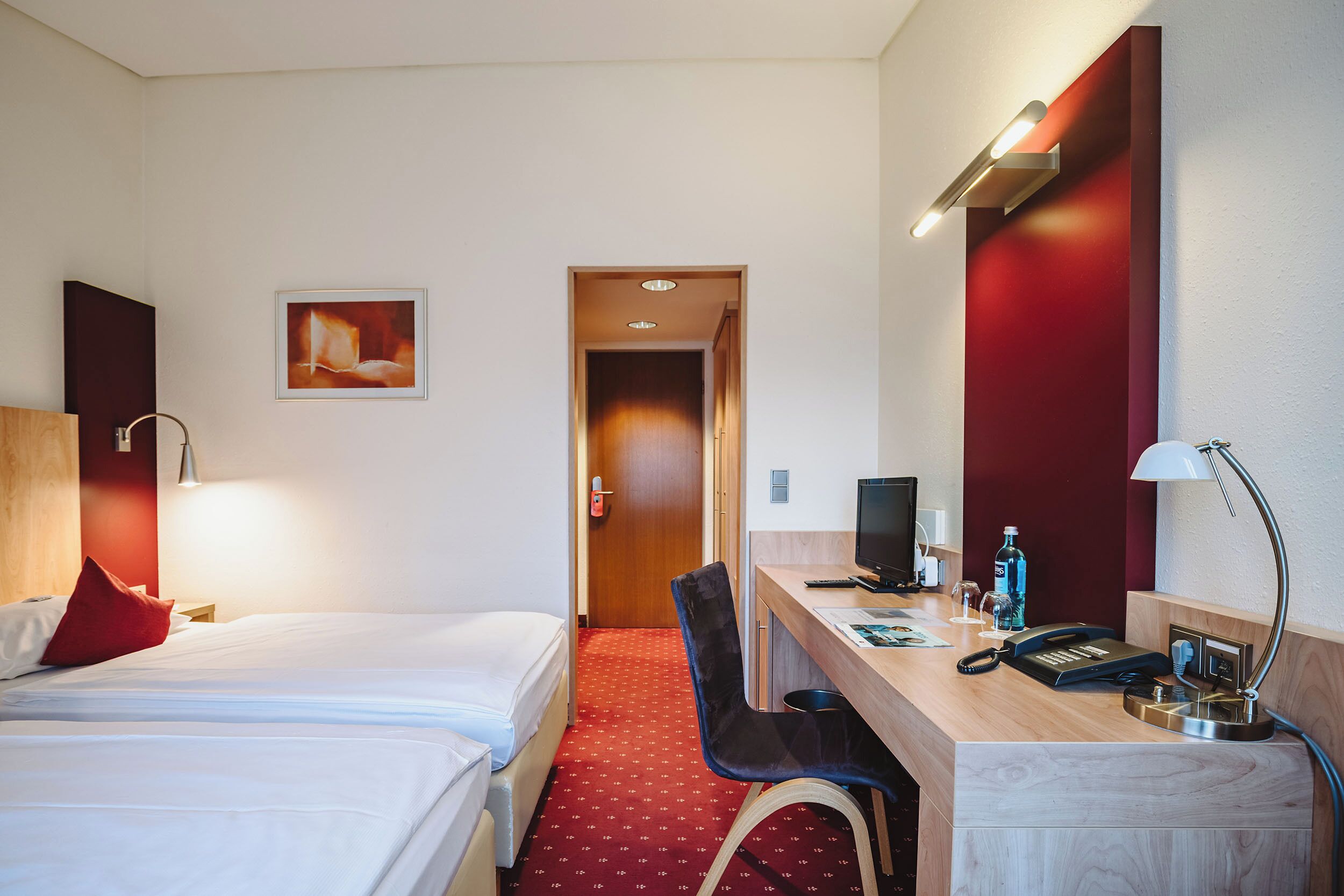 A hotel room with a bed, desk, chair, and a computer.