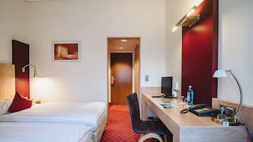 A hotel room with a bed, desk, chair, and a computer.