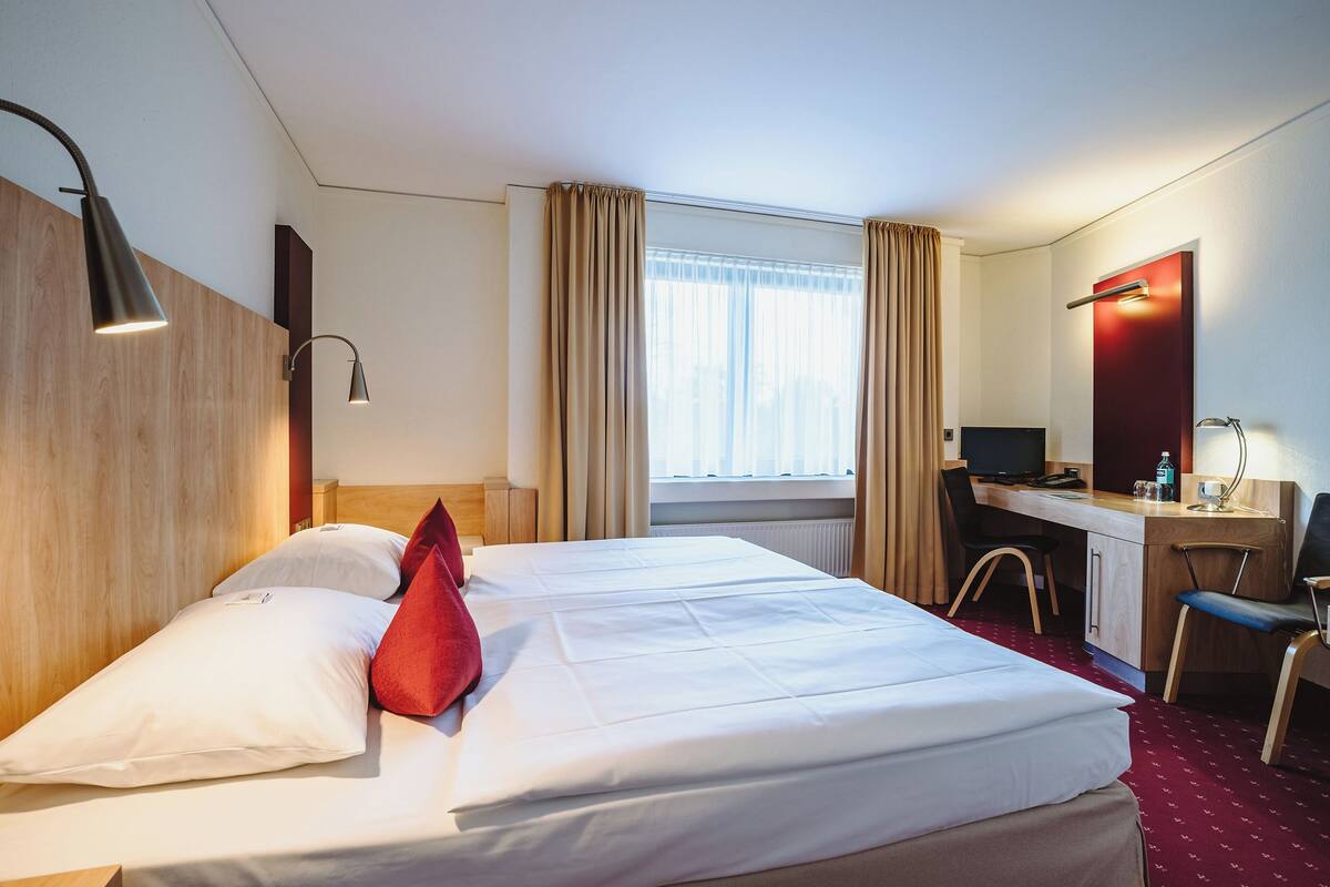 A hotel room with a bed, a desk, a chair, a TV, and a window with curtains.