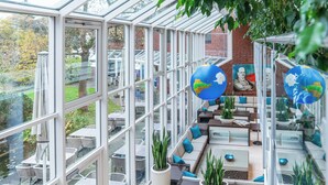 A spacious indoor area with glass walls, seating arrangements, and potted plants. - Hotel Gustav Stresemann Institut (Bonn)