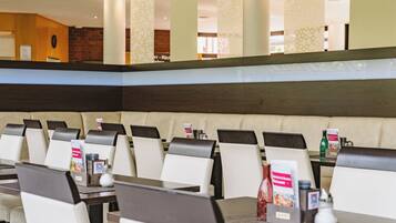 A hotel dining area with booth seating and tables, menus, condiments, and a brick wall in the background.