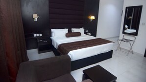 A modern hotel room with a large bed, a bedside table, a chair, a desk, and a mirror. - Hillsbay Hotels (Lekki)