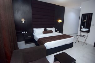 A modern hotel room with a large bed, a bedside table, a chair, a desk, and a mirror.