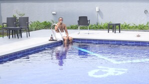 A man sitting by a pool with chairs and plants around. - Hillsbay Hotels (Lekki)