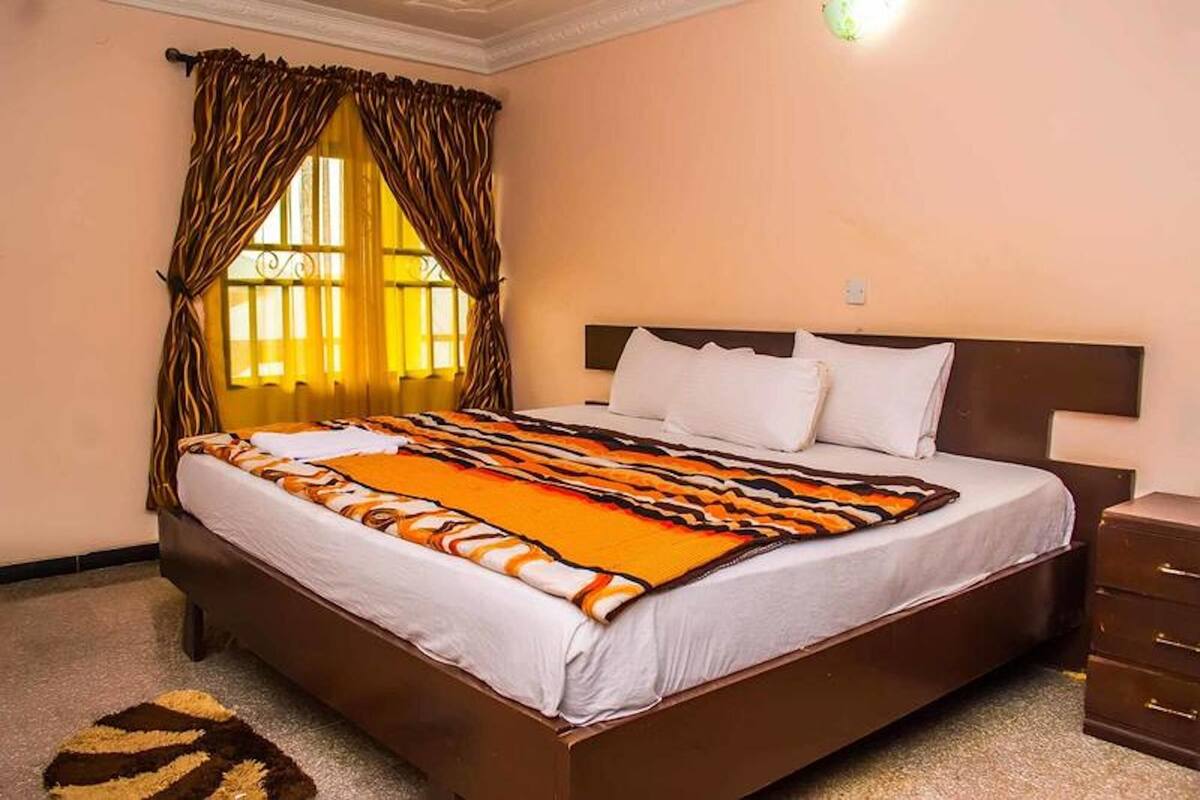 A neatly made bed with a patterned blanket, a bedside table, and a window with curtains.