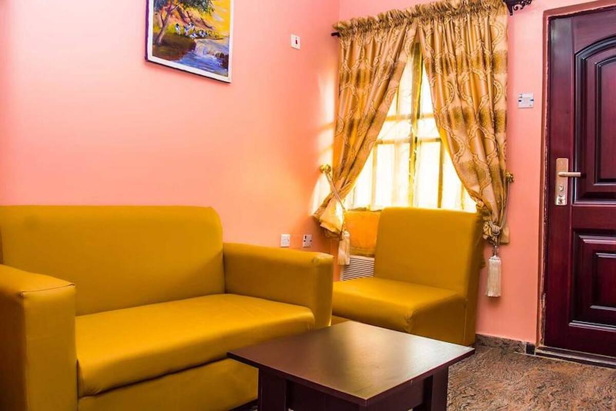 A room with a yellow sofa, a wooden coffee table, and a window with patterned curtains.