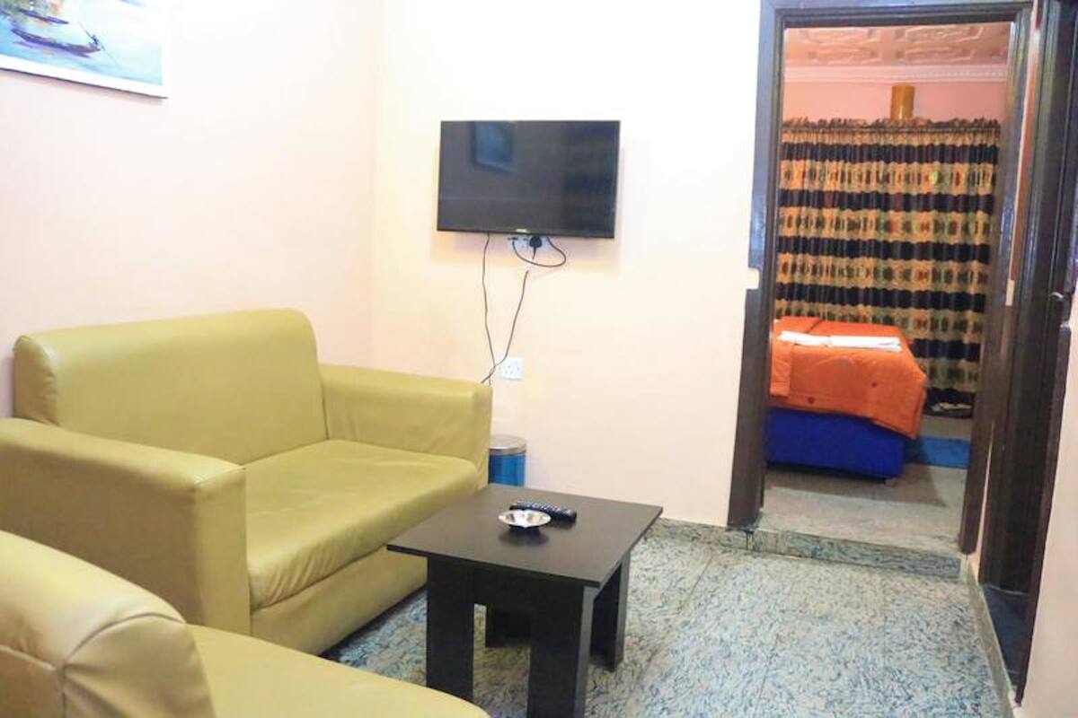 A room with a yellow sofa, a small black table, and a TV mounted on the wall.