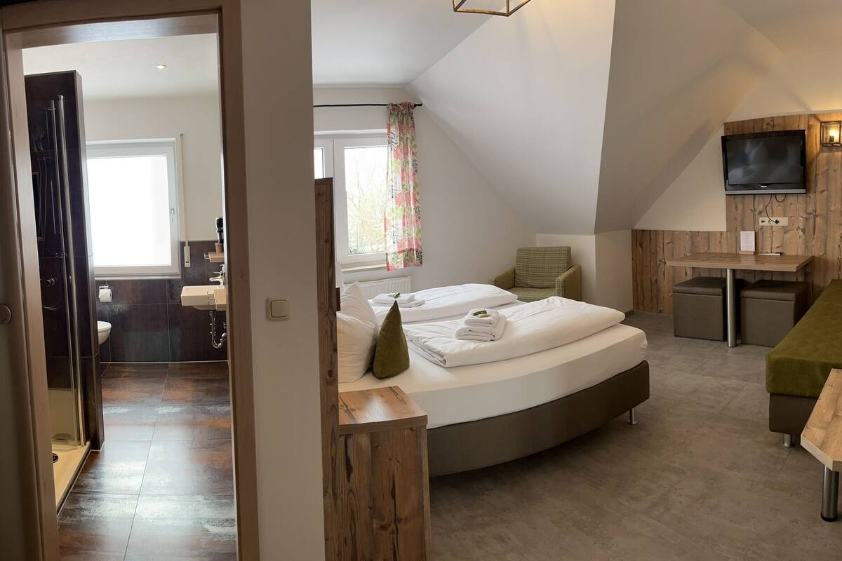 A modern hotel room with a curved bed, a small desk, a TV, and a seating area with cushions.