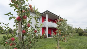 A red and white building with a balcony, surrounded by apple trees. - Landgasthaus Hofmann (Oberdachstetten)
