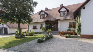 A traditional building with a tiled roof, a front porch with wooden chairs, and a well-maintained garden with various plants and flowers. - Landgasthaus Hofmann (Oberdachstetten)